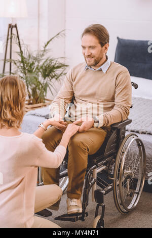 Heureux mari sur fauteuil roulant et épouse holding hands Banque D'Images