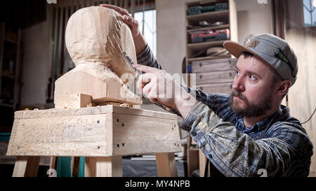 Jeune homme dans un menuisier scies vêtements de travail à la tête d'un homme avec un arbre , à l'aide d'un burin dans l'atelier, autour d'un lot d'outils pour le travail Banque D'Images