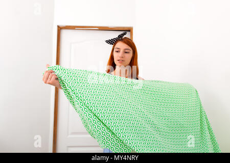 Сlose de jeunes femme en jeans et t-shirt noir nettoie le lit de vert-blanc literie géométrique dans une chambre avec des murs blancs et d'un coffre à dr Banque D'Images