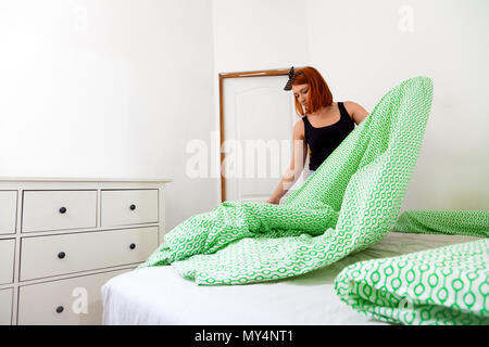 Сlose de jeunes femme en jeans et t-shirt noir ne ménage, supprime le lit avec géométrique vert et blanc et le linge de lit dans une chambre wifi Banque D'Images