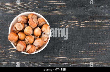 Bol en céramique blanche pleine de noisettes dans la coquille vide sur un fond de bois, vue du dessus Banque D'Images