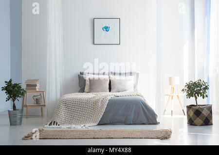 Couverture tricot sur gris lit dans chambre à coucher intérieur avec des plantes et de l'affiche. Photo réelle Banque D'Images