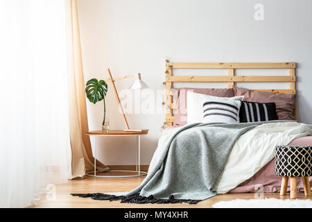 Tabouret à motifs à côté de lit avec tête de lit en bois à l'intérieur chambre à coucher avec lampe sur table. Photo réelle Banque D'Images