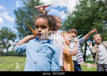 Les enfants jouent avec multiethnique adorable paper planes in park Banque D'Images