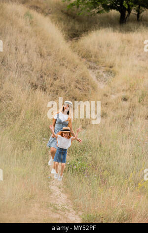 Heureuse mère et fille dans les chapeaux de paille à marcher ensemble on grassy hill Banque D'Images