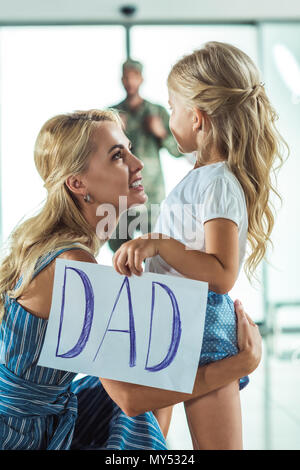 Portrait de Mère et fille en tenant la carte avec papa mot tout en répondant père en uniforme militaire à l'aéroport Banque D'Images