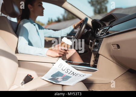 Jeune femme au volant d'une voiture avec des affaires journal allongé sur le siège avant Banque D'Images