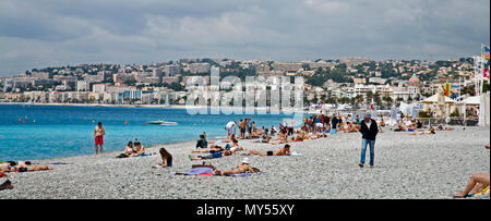 Nice, France- 2 juin 2016 : les gens se promener et se détendre et nager sur la plage en France sur une eau bleue et chaude journée avec des maisons derrière Banque D'Images