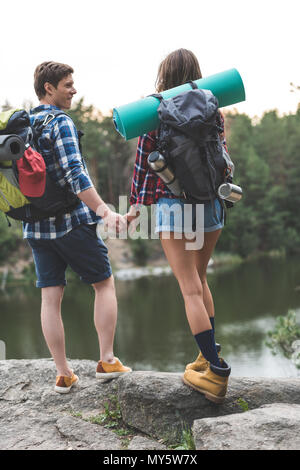 Young couple holding hands with Backpacks sur Rocky Lake Shore Banque D'Images