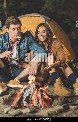 Couple heureux sur des bâtons de guimauve de torréfaction en voyage de camping Banque D'Images