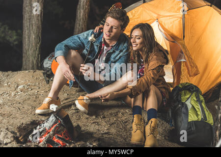 Torréfaction de couple sur des bâtons de guimauve en voyage de camping Banque D'Images