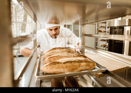 Le boulanger mettre les plateaux de pain frais sur le support à la fabrication Banque D'Images