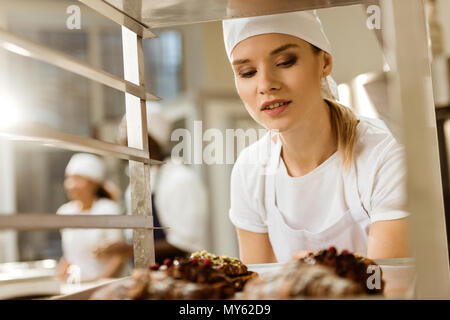 Belle femme Baker à la recherche au niveau du bac de croissants fraîchement cuits sur une plaque fabrication Banque D'Images