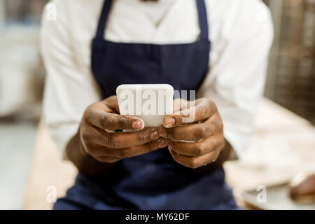 Cropped shot of african american Baker avec les mains couvertes de farine using smartphone Banque D'Images