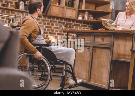 Portrait de femme avec homme handicapé en fauteuil roulant : cuire le dîner ensemble à la maison Banque D'Images