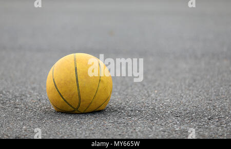 Main gauche focus, vieille déflaté laisser tomber sur une route de basket-ball jaune concept surafce. a besoin d'air usé, passé et jeter les équipements de sport. Banque D'Images