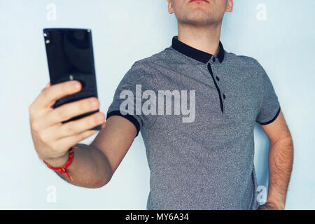 Guy prend lui-même sur un téléphone mobile. Un jeune homme prend un. un homme selfies Lecture des SMS sur un smartphone noir. Une personne regarde dans l'écran du téléphone sur bleu Banque D'Images