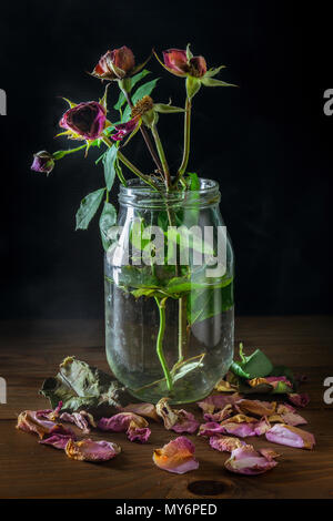 Nature morte avec roses fanées dans le vase en verre sur la table en bois Banque D'Images