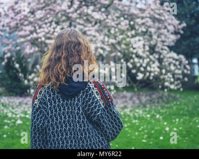 Une jeune femme se tient debout par un magnolia en fleurs dans le parc Banque D'Images