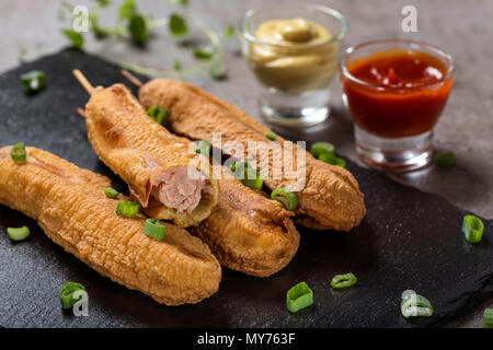 Quatre chiens de maïs frais o une ardoise foncé avec la sauce tomate et la moutarde - vue rapprochée Banque D'Images