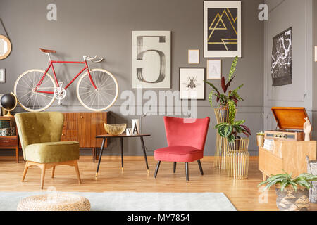 Intérieur chaleureux avec de confortables fauteuils vintage, de couleur rouge et verte par une petite table, un gramophone et des croquis sur le mur gris au moulage Banque D'Images