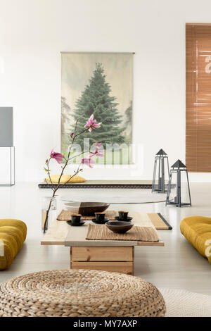 Close-up d'un pouf dans un salon intérieur avec une table à café, fleur de cerisier, lampes sur le plancher et un arbre poster Banque D'Images