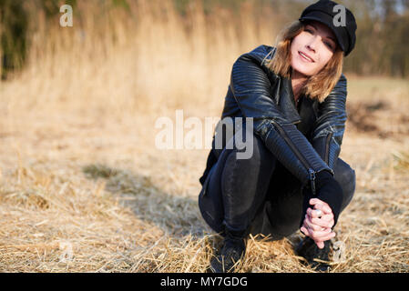 Cool woman wearing cap accroupi sur la paille sur le terrain, portrait Banque D'Images