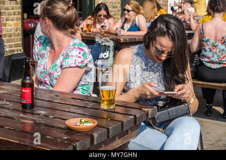 Les amis de s'asseoir ensemble dans un jardin mais s'ignorent, préférant d'interagir avec leurs téléphones mobiles. Banque D'Images