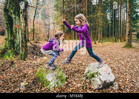 Les jumeaux identiques sont sauter de rochers dans la forêt sur la randonnée. Les enfants dans la forêt on active le trekking dans les montagnes sont sautant de roche en roche les reflets verts Banque D'Images