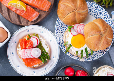 Du pain avec du fromage, l'oeuf et l'asperge, un autre pain avec le saumon et les asperges.. Alimentation saine. Délicieux petit-déjeuner. Fond gris. Mise à plat Banque D'Images