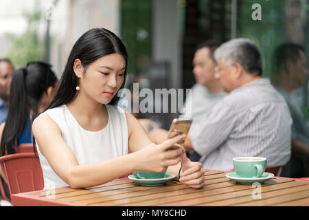 Businesswoman sitting outdoors, au cafe, using smartphone Banque D'Images