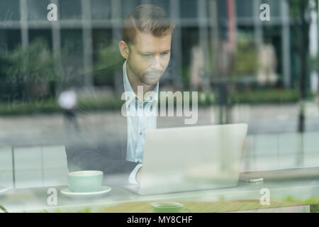 Businessman sitting in cafe, using laptop, vu à travers la vitre Banque D'Images