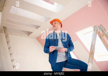 Portrait of construction worker using digital tablet en étant debout sur l'échelle à la construction site. Banque D'Images