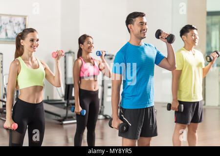 Handsome man smiling fit alors que l'exercice de biceps lors d'entraînement de groupe Banque D'Images
