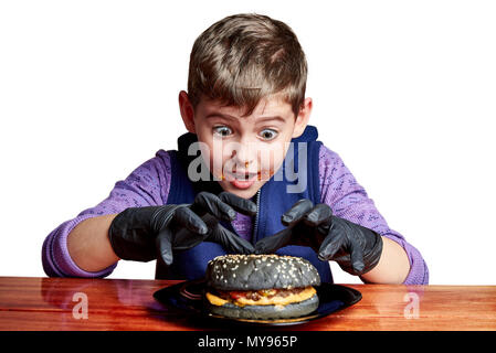 Gants noirs en garçon manger émotionnellement un burger à la table sur un fond blanc Banque D'Images