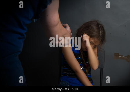 Un adulte homme fort punit une petite fille avec des nattes, qui, à son avis, est à blâmer pour le mur gris sale Banque D'Images