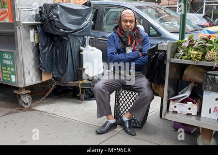 Un musulman vendeur de légumes dans une profonde réflexion sur la 37e Avenue à Jackson Heights, Queens, New York. Banque D'Images