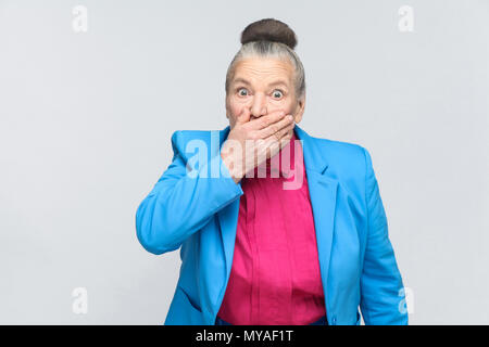 Peur de femme et bouche fermée ont des gros yeux. Portrait de grand-mère expressive avec costume bleu clair et rose shirt debout avec recueillies bun g Banque D'Images