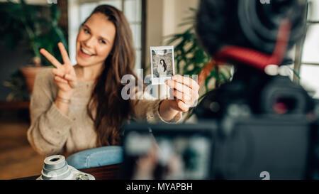 Femme montrant une photographie prise à l'aide d'un appareil photo instantané et la victoire même si l'enregistrement vidéo du contenu pour son blog à la maison. Blogger enregistremen Banque D'Images