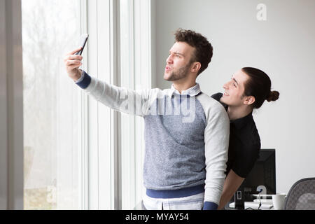 Deux jeunes entrepreneurs font faces stupides tout en prenant vos autoportraits dans un bureau moderne. Banque D'Images