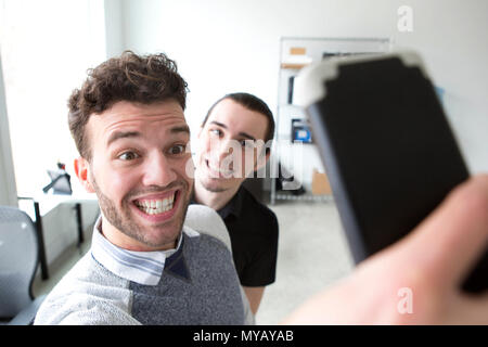 Deux jeunes entrepreneurs font faces stupides tout en prenant vos autoportraits dans un bureau moderne. Banque D'Images