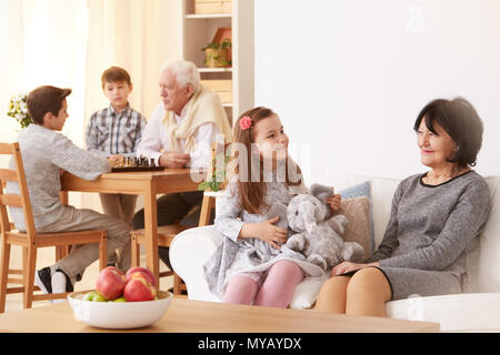 Petite fille parler avec grand-mère dans la salle de séjour et le grand-père jouer aux échecs avec petits-fils Banque D'Images