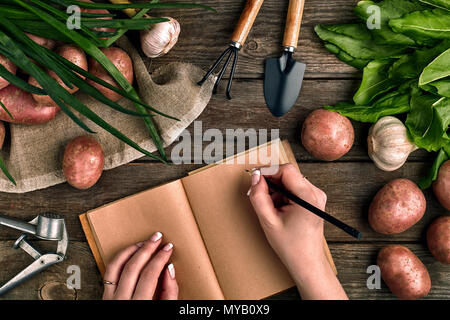 Le bloc-notes pour les inscriptions de femmes, Close-up. Vue d'en haut sur un fond de bois avec les outils de jardin, les verts, les oignons, l'ail et les pommes de terre Banque D'Images