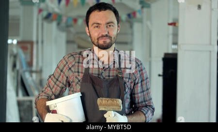 Heureux jeune homme barbu avec peintre peut peindre et pinceau standing and smiling Banque D'Images