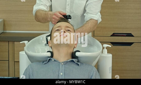 Bel homme ayant ses cheveux lavés dans de coiffure. Jeune homme couché avec ses yeux fermés en salon de beauté. Banque D'Images