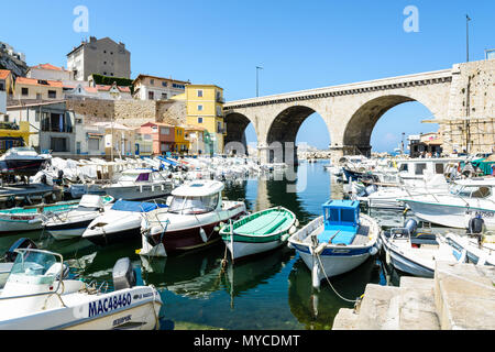 Le petit port de pêche du Vallon des Auffes par un matin ensoleillé avec des bateaux traditionnels et modernes, cabanons et le pont routier à l'arrière-plan. Banque D'Images