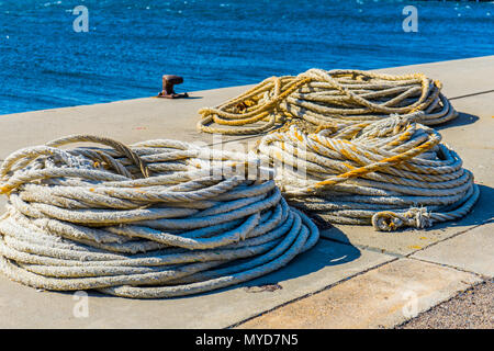 De longues cordes allongé sur le sol dans un port avec l'océan et un point d'ancrage visible dans l'arrière-plan. Banque D'Images