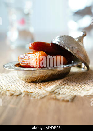 Dates de fruits frais dans un bol en métal argenté sur un morceau de sacs sur table en bois de noyer Banque D'Images