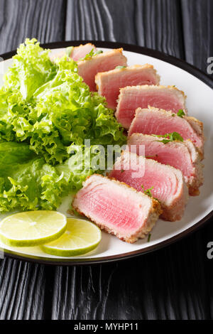 Délicieux steak de thon ahi dans la chapelure panko avec de la laitue et de la chaux libre sur une plaque sur une table verticale noire. Banque D'Images