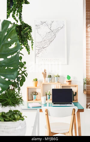 White Président Comité permanent par un simple bureau en bois avec cactus, tasse à café, ordinateur portable et ordinateur portable à l'intérieur du bureau d'accueil lumineux avec map poster Banque D'Images